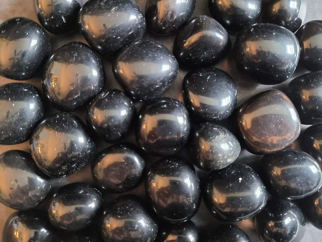 A overhead image of gumball-sized Apache Tear obsidian tumble stones - used for grounding, grief support, and gentle emotional healing.