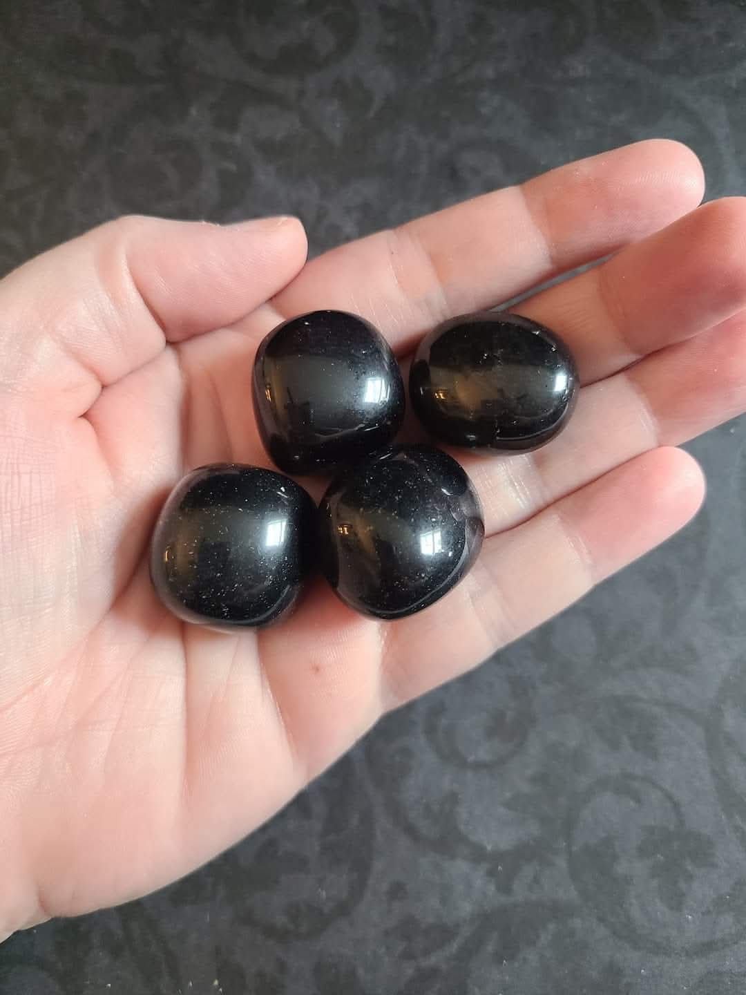 A hand holding a gumball-sized Apache Tear obsidian tumble stone - used for grounding, grief support, and gentle emotional healing.