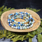 Azurite, hackmanite and chrysocolla crystal/mineral beaded bracelet on a wooden dish with green foliage on a dark background