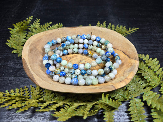 Azurite, hackmanite and chrysocolla crystal/mineral beaded bracelet on a wooden dish with green foliage on a dark background