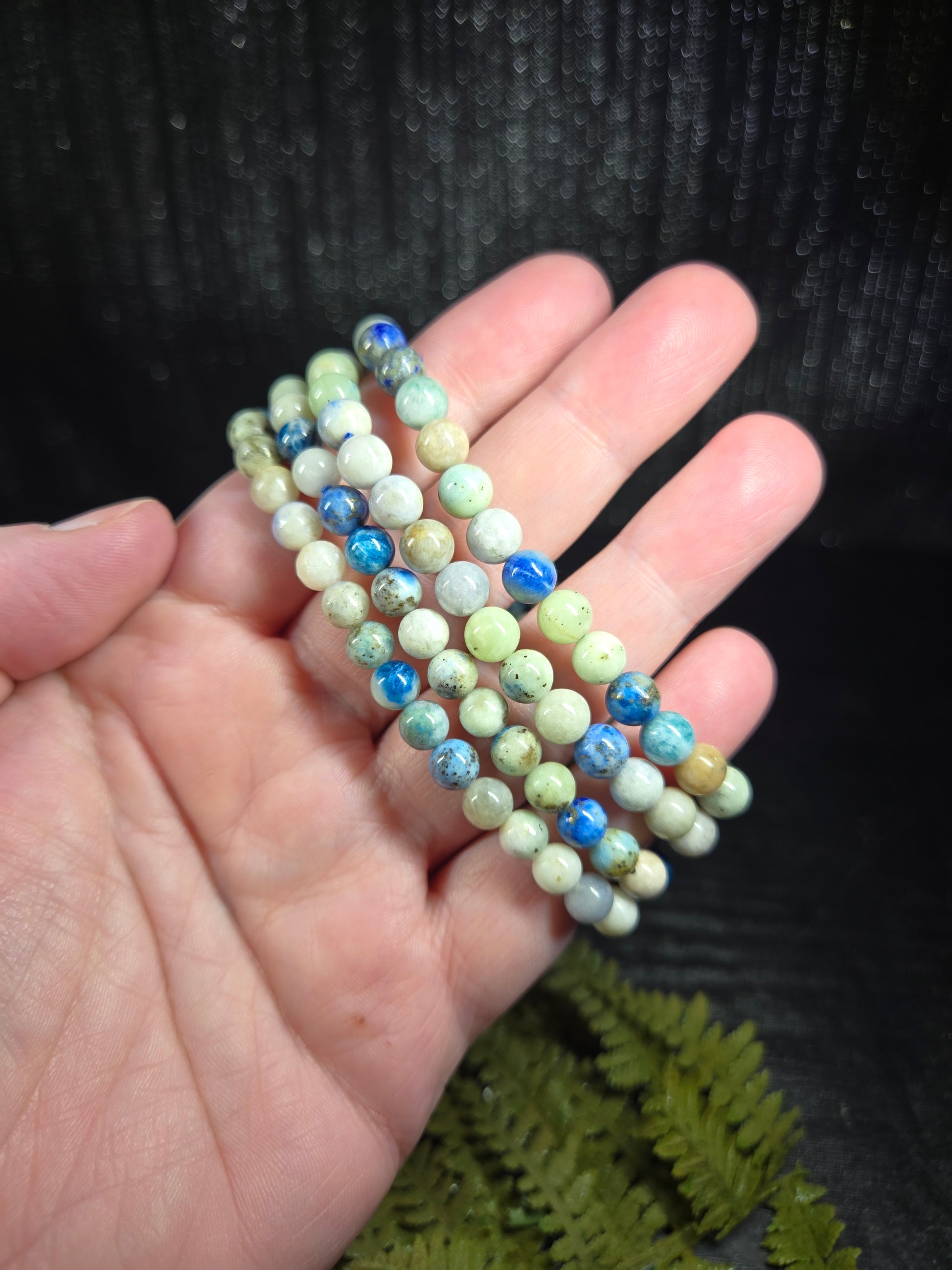 A hand holding 4 strings of Azurite, hackmanite and chrysocolla crystal/mineral beaded bracelets