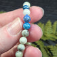 A hand holding a string of Azurite, hackmanite and chrysocolla crystal/mineral beaded bracelet