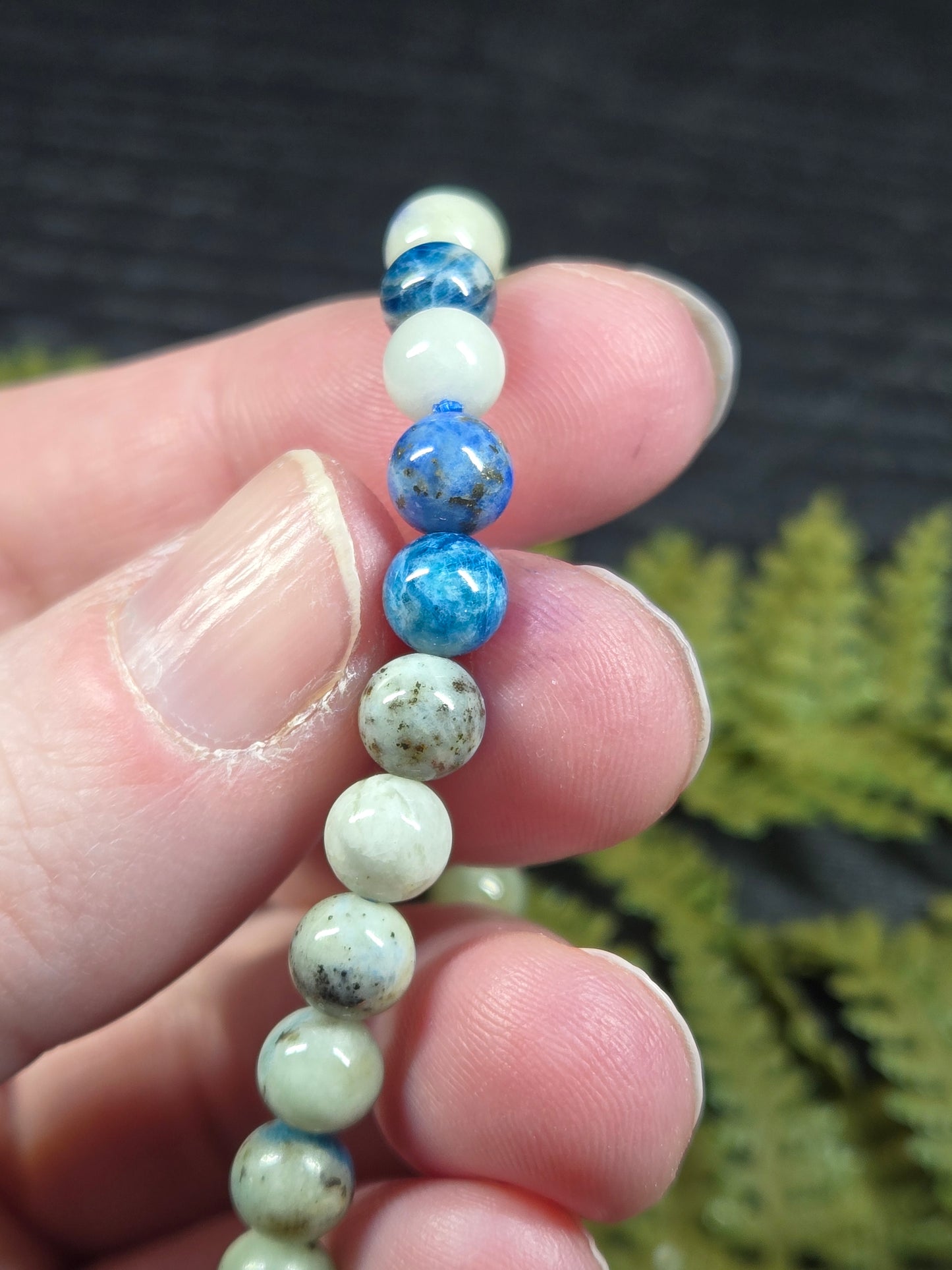 A hand holding a string of Azurite, hackmanite and chrysocolla crystal/mineral beaded bracelet