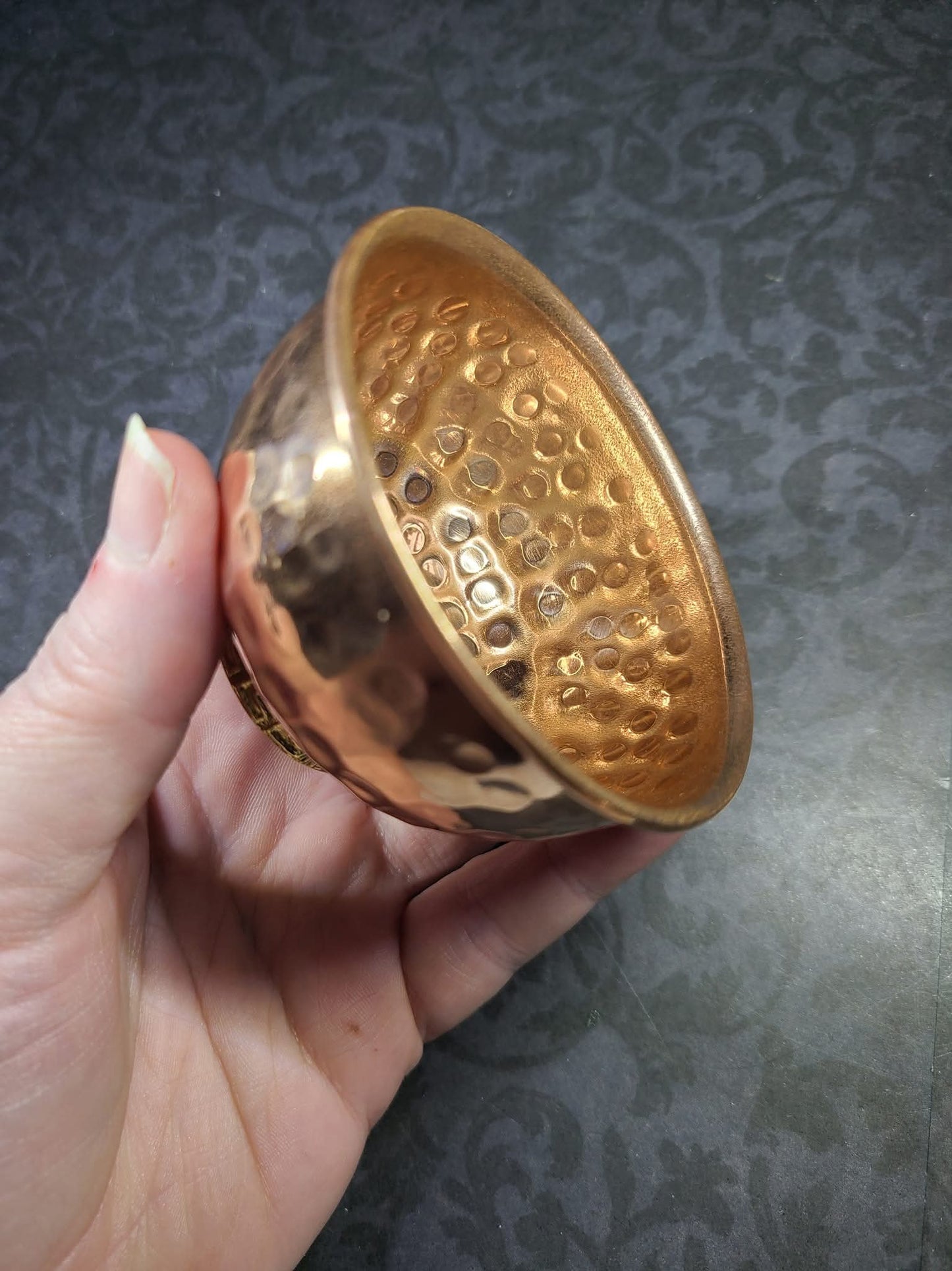 Hand holding a copper bowl with textured interior against a dark patterned background - Dark Star Curiosities